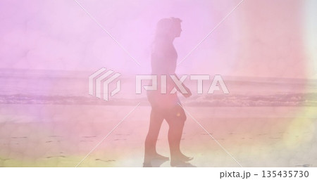 Walking adult woman wearing tank top and shorts along sandy shoreline at beach, pastel reflection 135435730