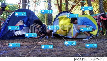 Group of friends assembling blue and yellow dome tents in pine forest, with social media icons 135435787