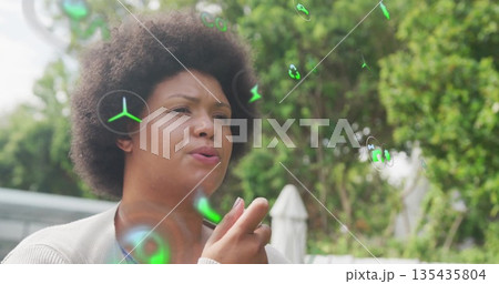 Holding device, woman wearing cardigan watching floating green holographic symbols on garden patio 135435804