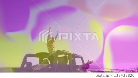 Friends raising arms and leaning from open-top jeep on rocky shoreline, with colored bokeh overlays Friends raising arms and leaning from open-top jeep on rocky shoreline, with colored bokeh overlays 135435820