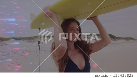 Woman wearing dark swimsuit holding yellow surfboard on sandy shore, smiling near dunes, surf leash 135435822