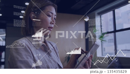 Analyzing business professional wearing blouse holding tablet in office, with floating data graphs Analyzing business professional wearing blouse holding tablet in office, with floating data graphs 135435829