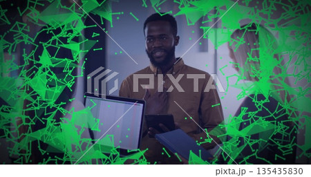 Presenting man in brown shirt speaking, gesturing, holding tablet in office, with network graphics 135435830
