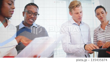 Reviewing team wearing formal attire examining reports and tablet at table in conference area 135435874