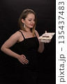 A woman in a black dress blows out a candle on a bento cake. Smoke on a black background. A girl's birthday, happiness, a gift. High quality photo 135437483