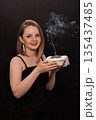 A woman in a black dress blows out a candle on a bento cake. Smoke on a black background. A girl's birthday, happiness, a gift. High quality photo 135437485