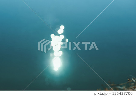 Sunlight reflecting on calm blue water with gentle ripples and abstract bokeh 135437700