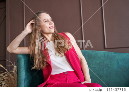 Young caucasian woman in stylish pink suit posing confidently on green sofa 135437716