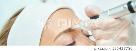 Close-up of female receiving eyebrow tattoo procedure by professional cosmetic 135437756