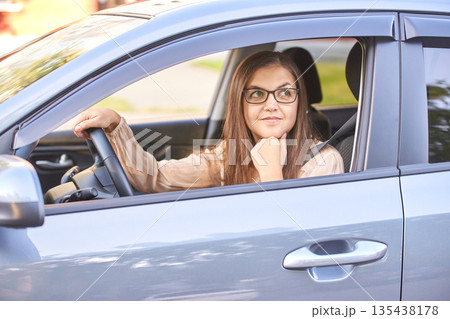 Young caucasian woman driving car with smile while looking out window Young caucasian woman driving car with smile while looking out window 135438178