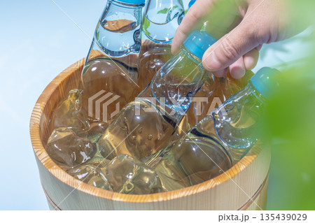 氷で冷やした木桶のビー玉入りガラス瓶のラムネを手に取る夏 氷で冷やした木桶のビー玉入りガラス瓶のラムネを手に取る夏 135439029