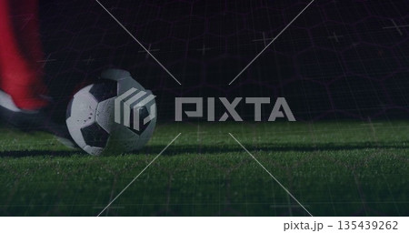Resting classic soccer ball beneath red sock and black cleat on night pitch, with digital grid Resting classic soccer ball beneath red sock and black cleat on night pitch, with digital grid 135439262