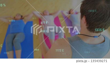 Leading male instructor guiding women crunching on mats in studio with currency overlay, copy space 135439271