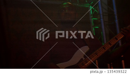 Performing adult male musician playing bass guitar on dark stage with green LED and red glow 135439322
