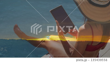 Woman in red swimsuit, straw hat holding tablet and dipping legs at pool edge, copy space 135439558