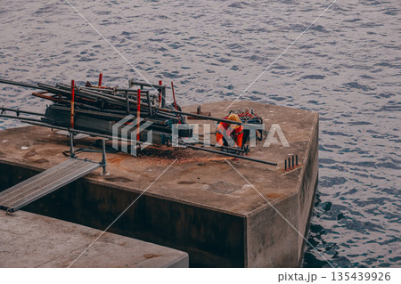 Dec 31 2025 Worker In Orange Safety Gear On Concrete Pier By The Sea Dec 31 2025 Worker In Orange Safety Gear On Concrete Pier By The Sea 135439926