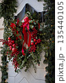 Holiday wreath with red ornaments and ribbons adorned with greenery on a white wall 135440105