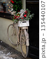 Vintage bicycle decorated with Christmas greenery and ornaments against a dark wall 135440107