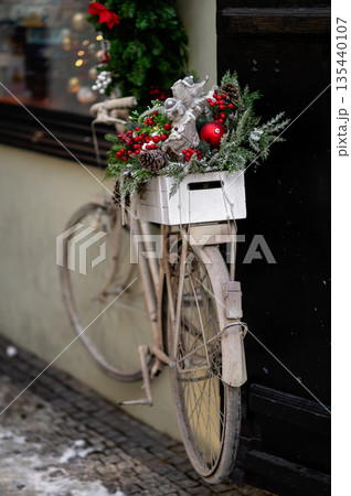 Vintage bicycle decorated with Christmas greenery and ornaments against a dark wall 135440107