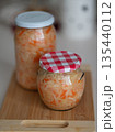 Jars of fermented sauerkraut with carrots on wooden cutting board in kitchen setting 135440112