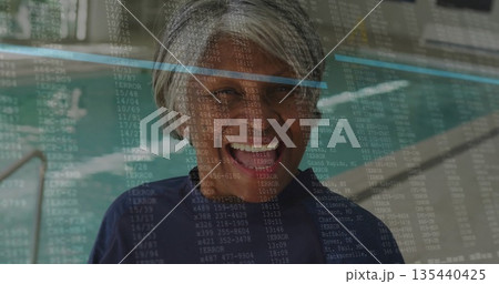 Standing senior woman wearing navy swim shirt on pool deck by steel ladder, digital code overlay Standing senior woman wearing navy swim shirt on pool deck by steel ladder, digital code overlay 135440425