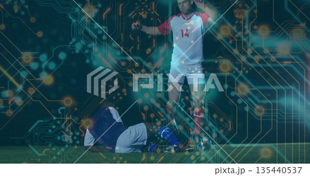 Competing soccer player in red-white kit tackling rival on field under lights, with circuit overlay Competing soccer player in red-white kit tackling rival on field under lights, with circuit overlay 135440537