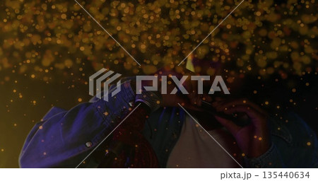 Playing musician in denim jacket blowing harmonica at microphone stand on dark stage, golden bokeh 135440634