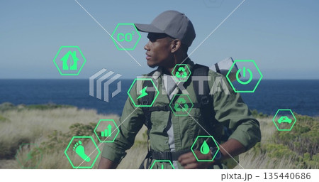 Standing hiker wearing baseball cap and olive jacket on coast, with backpack and mat, green icons 135440686
