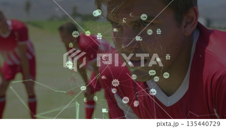 Bending adult in red jersey catching breath on grass field, with digital overlay icons, copy space 135440729