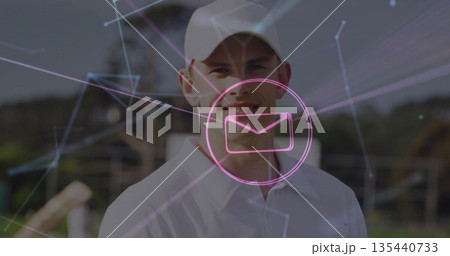 Standing man in baseball cap, shirt showing magenta envelope icon and network lines in rural field 135440733