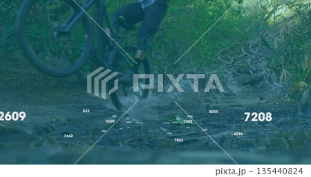 Propelling biker wearing shorts and blue shirt splashing through shallow forest stream, water spray 135440824