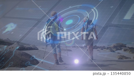 Walking mature hiking couple crossing sandy shore, with backpacks, boots, poles and AR charts 135440850