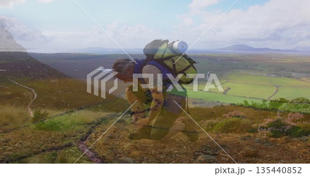 Kneeling adult hiker tying boot laces on mountain trail, with hiking backpack and valley view 135440852
