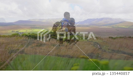 Standing couple of hikers overlooking valley from grassy hillside, with backpacks and rolled mat 135440857