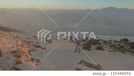 Walking female hiker traversing rocky coastal beach, with poles backpack boots, copy space 135440858