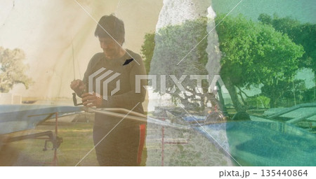 Adjusting senior fisher tightening fishing reel on metal rod rack by lake, with lounge chairs 135440864