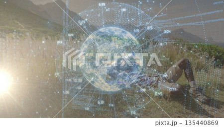 Lying hiker in boots viewing holographic globe data among tall meadow grasses at sunset, copy space 135440869
