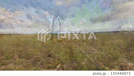 Traversing hiker wearing wide-brimmed hat on semi-arid plain, with backpack and trekking pole 135440873