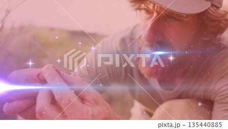 Crouching researcher wearing cap and shirt examining small lizard at sunlit scrub, lens flare Crouching researcher wearing cap and shirt examining small lizard at sunlit scrub, lens flare 135440885