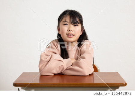 机の上で腕を組んでカメラ目線で微笑む小学生の女の子 机の上で腕を組んでカメラ目線で微笑む小学生の女の子 135442972