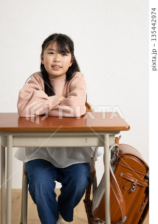 机の上で腕を組んでカメラ目線で微笑む小学生の女の子 机の上で腕を組んでカメラ目線で微笑む小学生の女の子 135442974