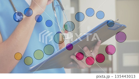 Nurse in blue scrubs reviewing notes on blue clipboard in clinic room, wearing stethoscope 135443013