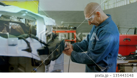 Mechanic wearing coveralls and goggles grinding front-end with grinder in workshop, copy space Mechanic wearing coveralls and goggles grinding front-end with grinder in workshop, copy space 135443148