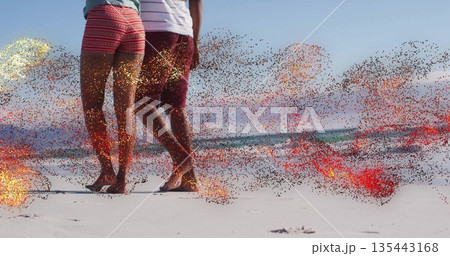 Walking barefoot couple wearing patterned shorts and striped Tshirt leaving footprints on beach 135443168