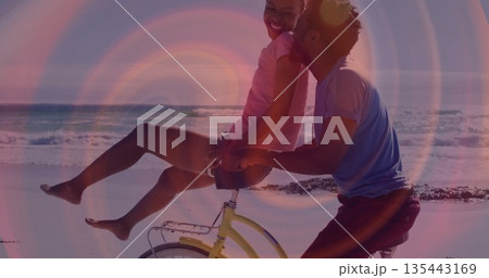 Pedaling romantic couple riding yellow bicycle along wet sandy shore, with ocean waves rolling Pedaling romantic couple riding yellow bicycle along wet sandy shore, with ocean waves rolling 135443169