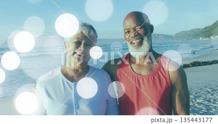 Smiling mature couple sharing affectionate moment on sandy beach by ocean, with bokeh light effects 135443177