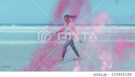Walking barefoot woman in white tee and jeans along shallow shoreline, with pink powder splashes 135443189