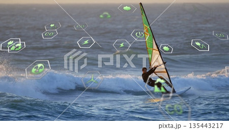 Cutting windsurfer in black wetsuit skimming sailboard on swells near sunset, hex icons, copy space 135443217