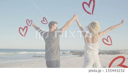Raising arms and holding hands couple wearing beachwear on beach, ocean waves, red heart doodles 135443232