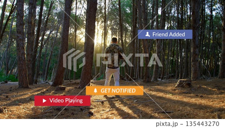 Viewing notification overlays, man in camouflage shirt holding smartphone at pine forest clearing 135443270